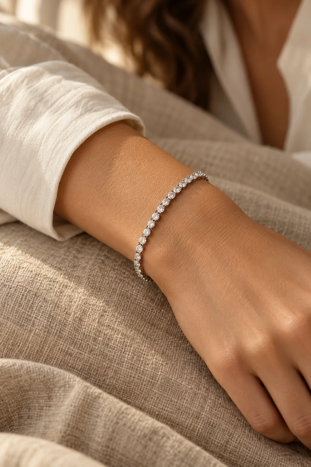 A wrist resting on linen, wearing a white gold diamond tennis bracelet